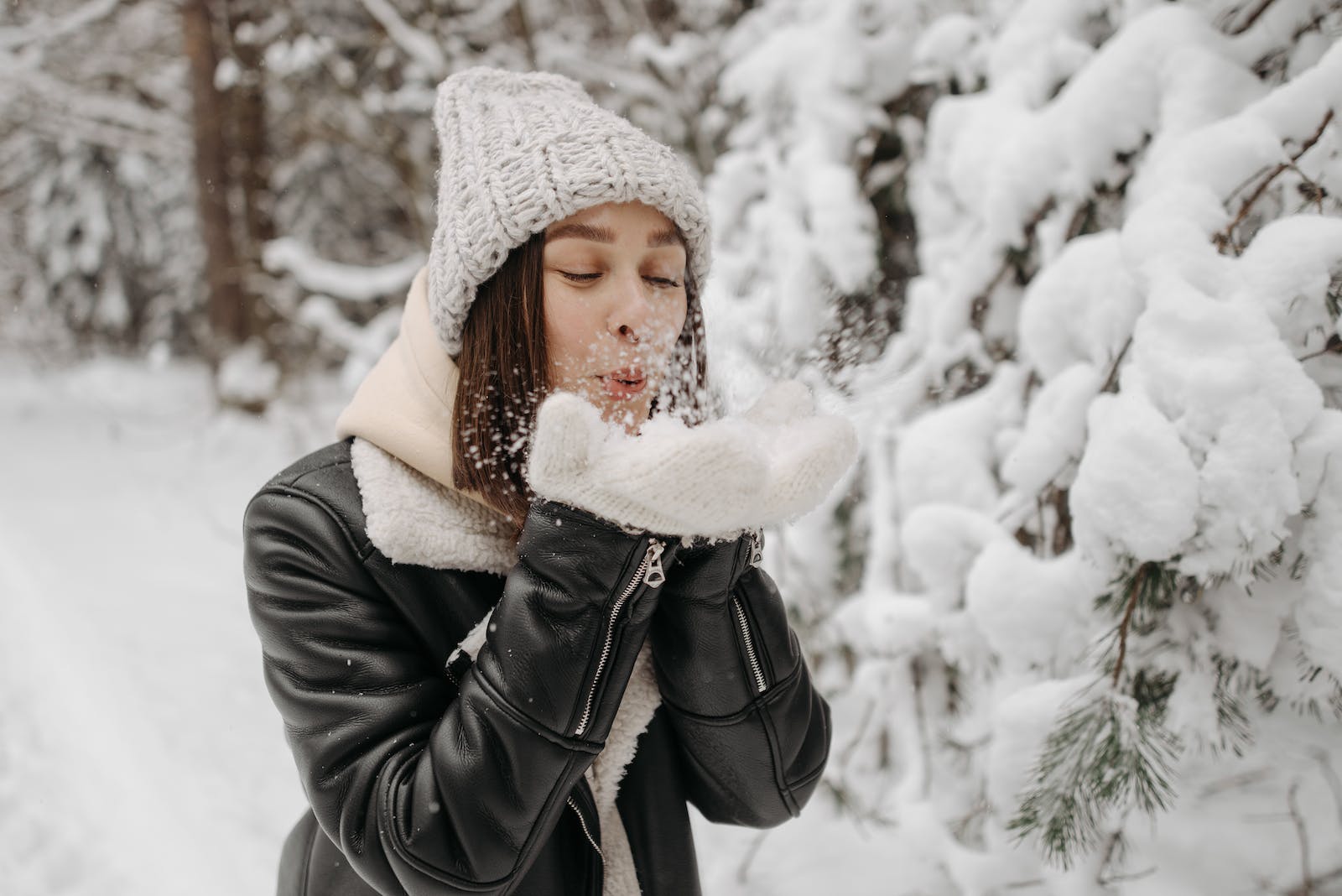 Photo of a Woman in a Black Leather Jacket Blowing Snow on Her Hands